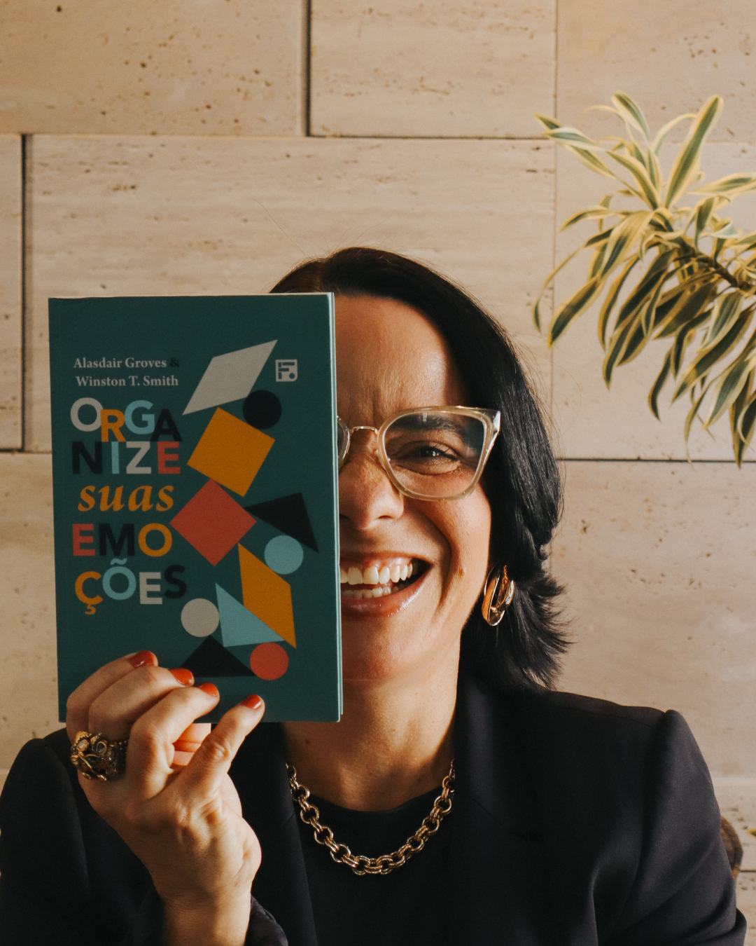 Psicóloga Flávia Siqueira sorrindo e segurando um livro sobre emoções